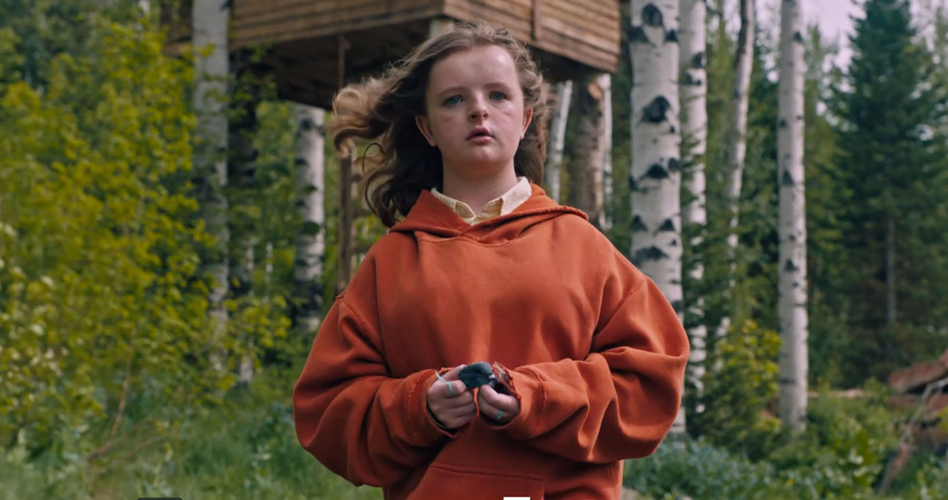 A white preteen girl in an oversized orange hoodie considering something in the distance