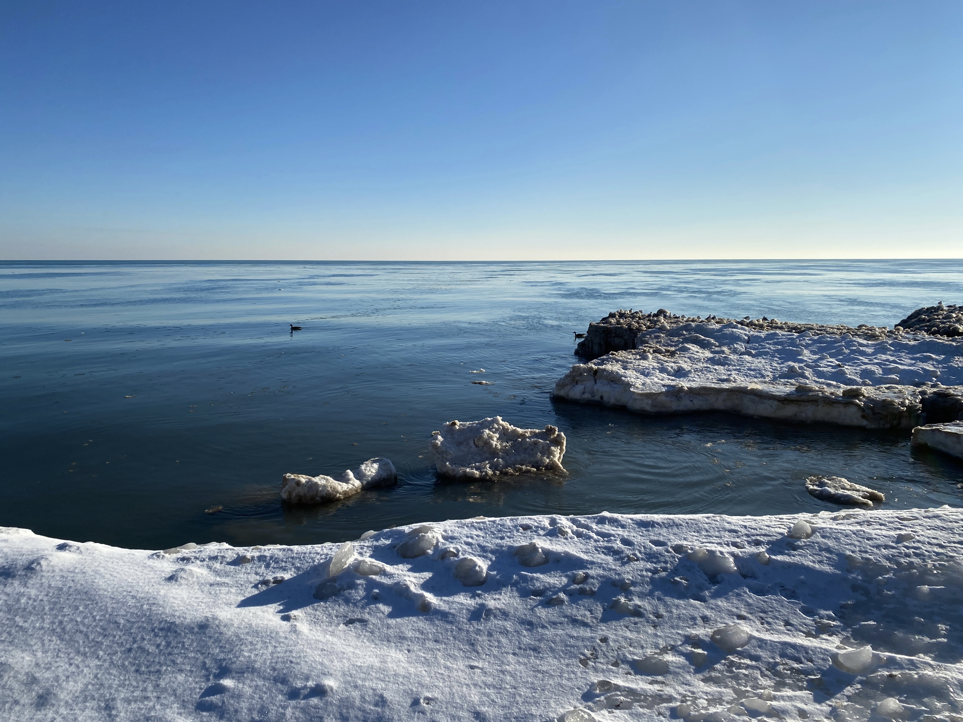 Horizon of large Lake Michigan with deep blue sky overhead and floes of ice in the foreground