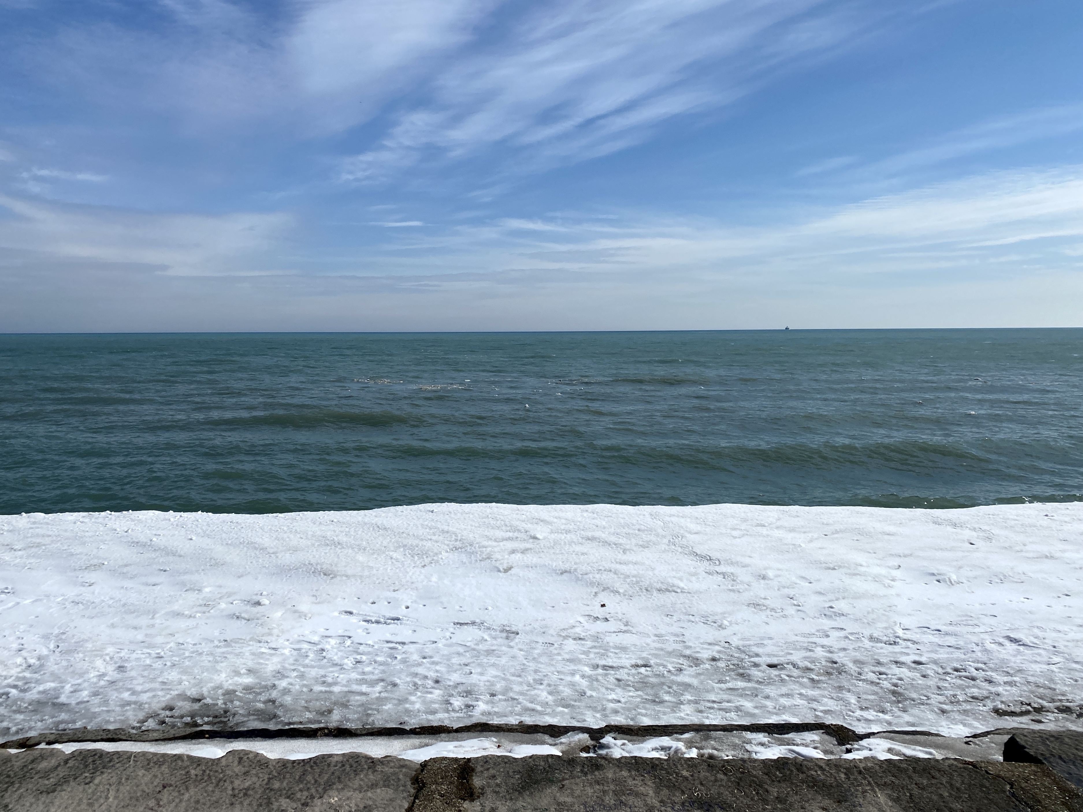 Horizon of large Lake Michigan with clear blue sky overhead, turquoise-shaded water and a shelf of snow in the foreground
