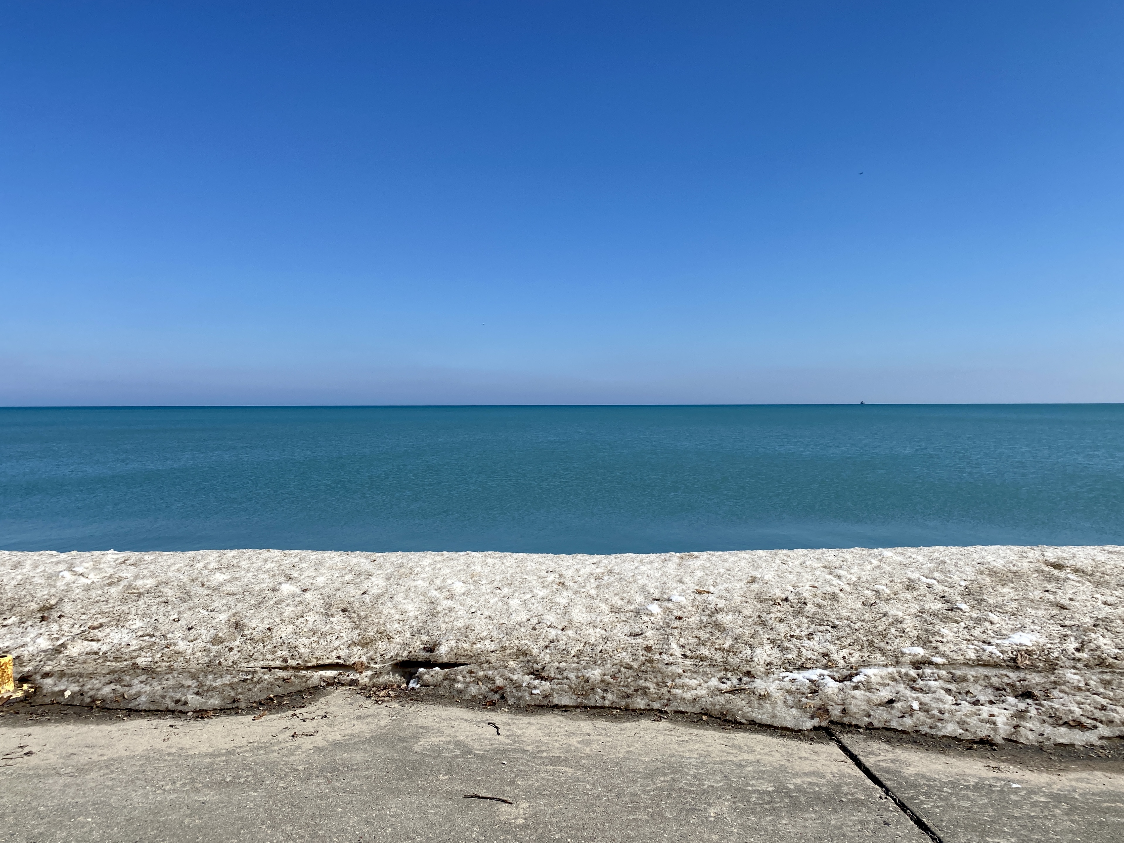Horizon of large Lake Michigan with clear, deep blue sky, deep turquoise water and a shelf of snow in the foreground