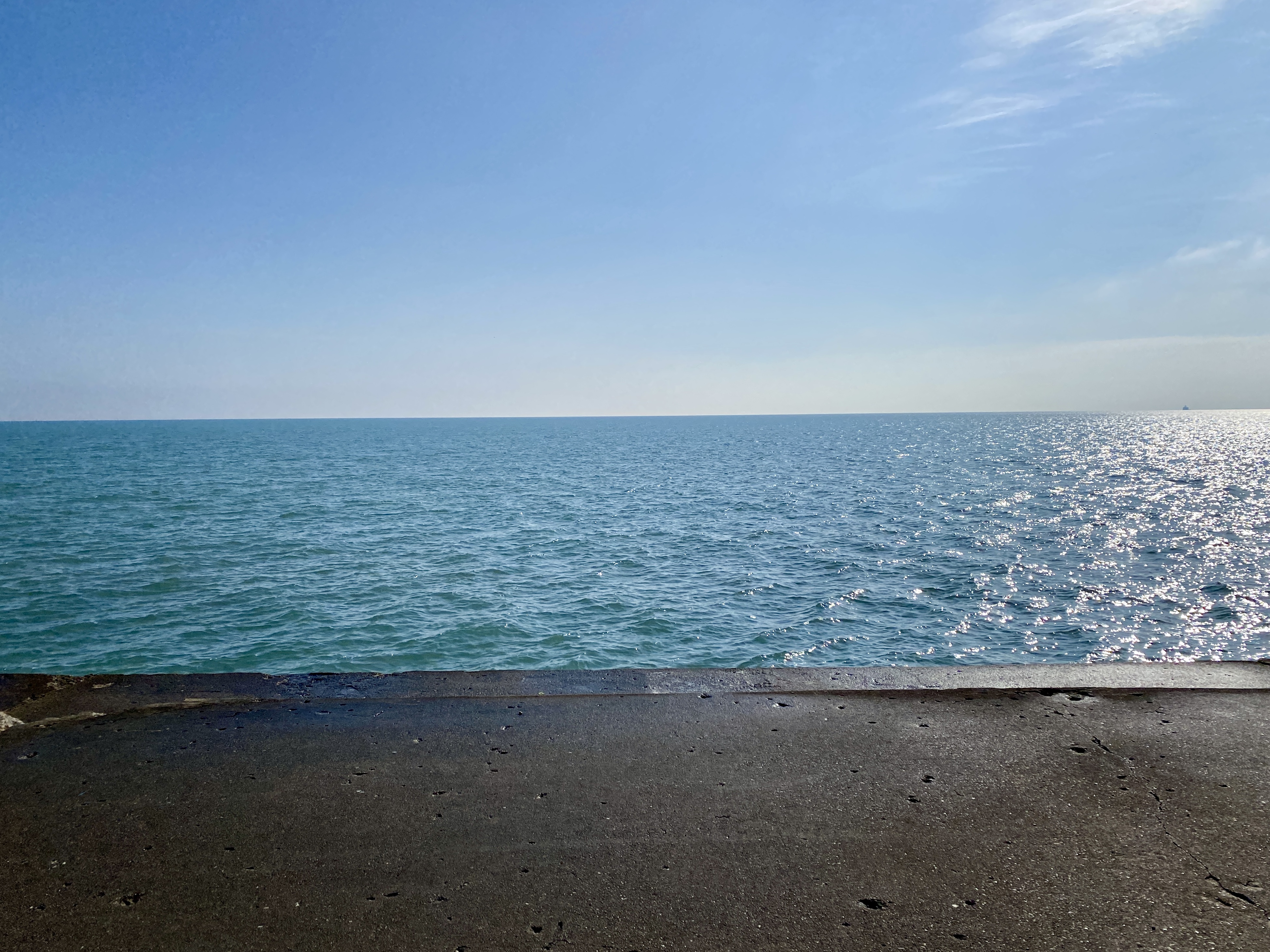 Horizon of large Lake Michigan with a hazy blue sky overhead and a concrete shelf in the foreground