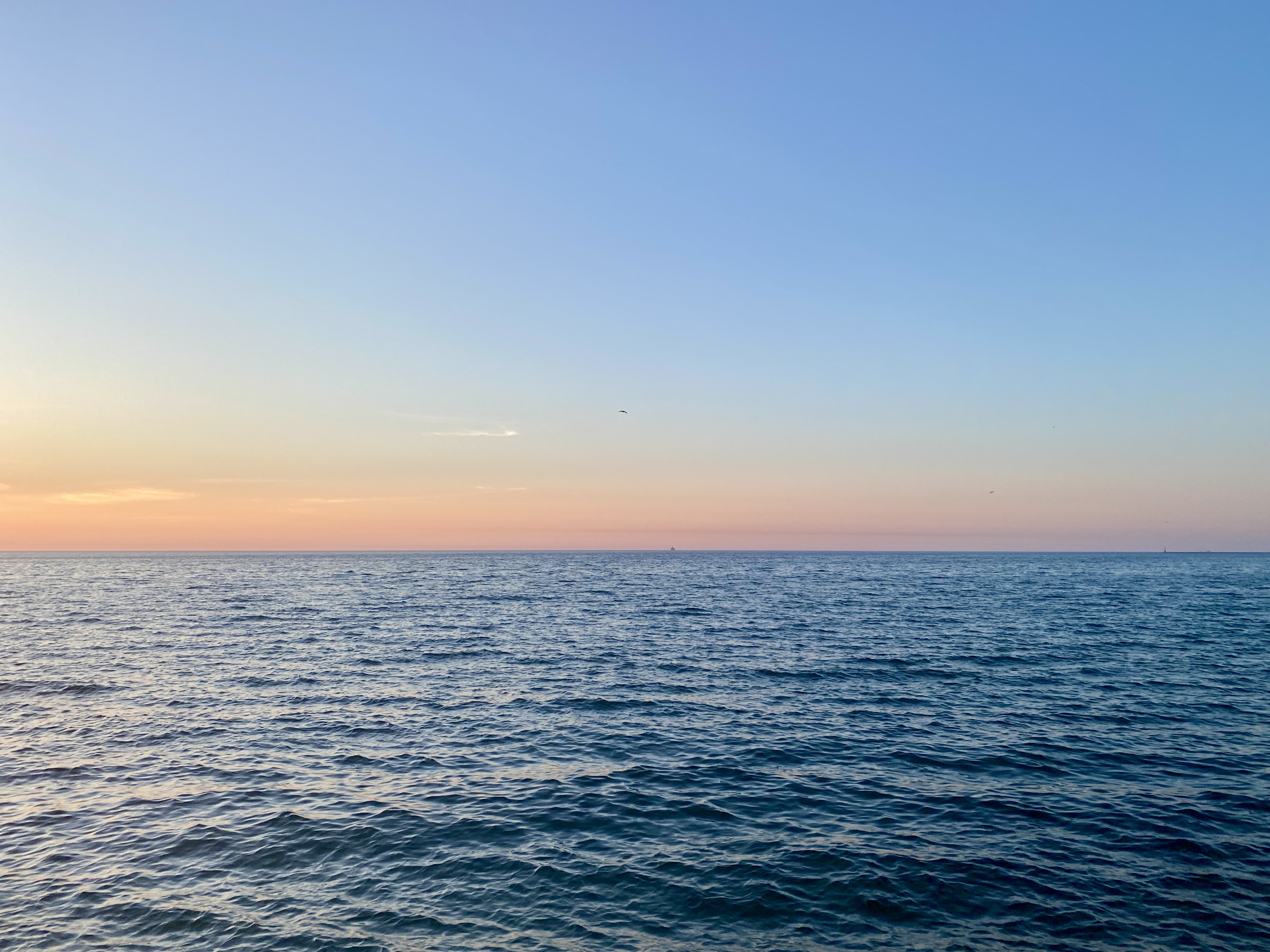 Horizon of large lake at sunrise, water shaded dark blue and sky fading from pink to deep blue above
