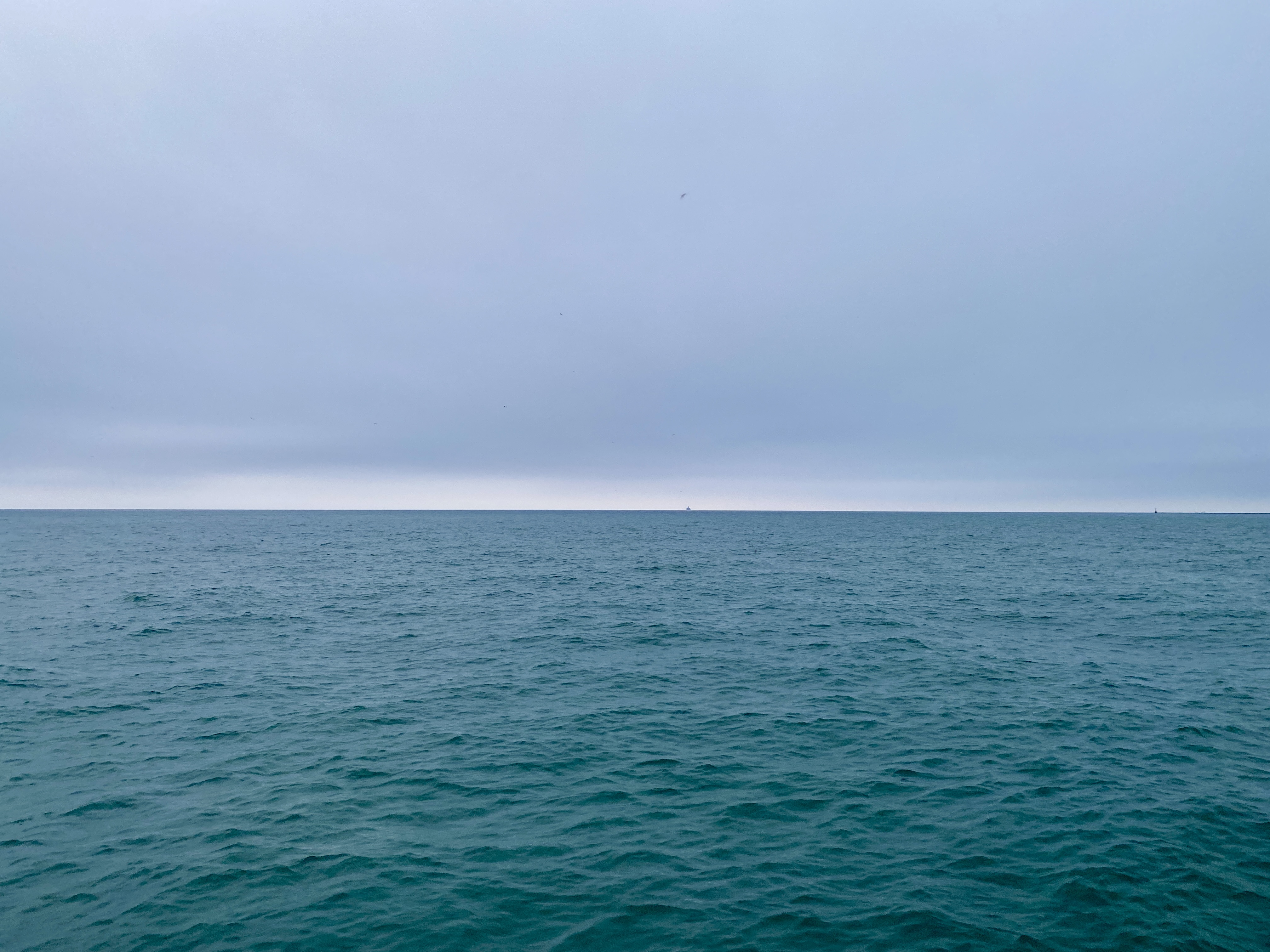 Horizon of large lake under a grey clouded sky, water moderately calm and shaded deep turquoise blue