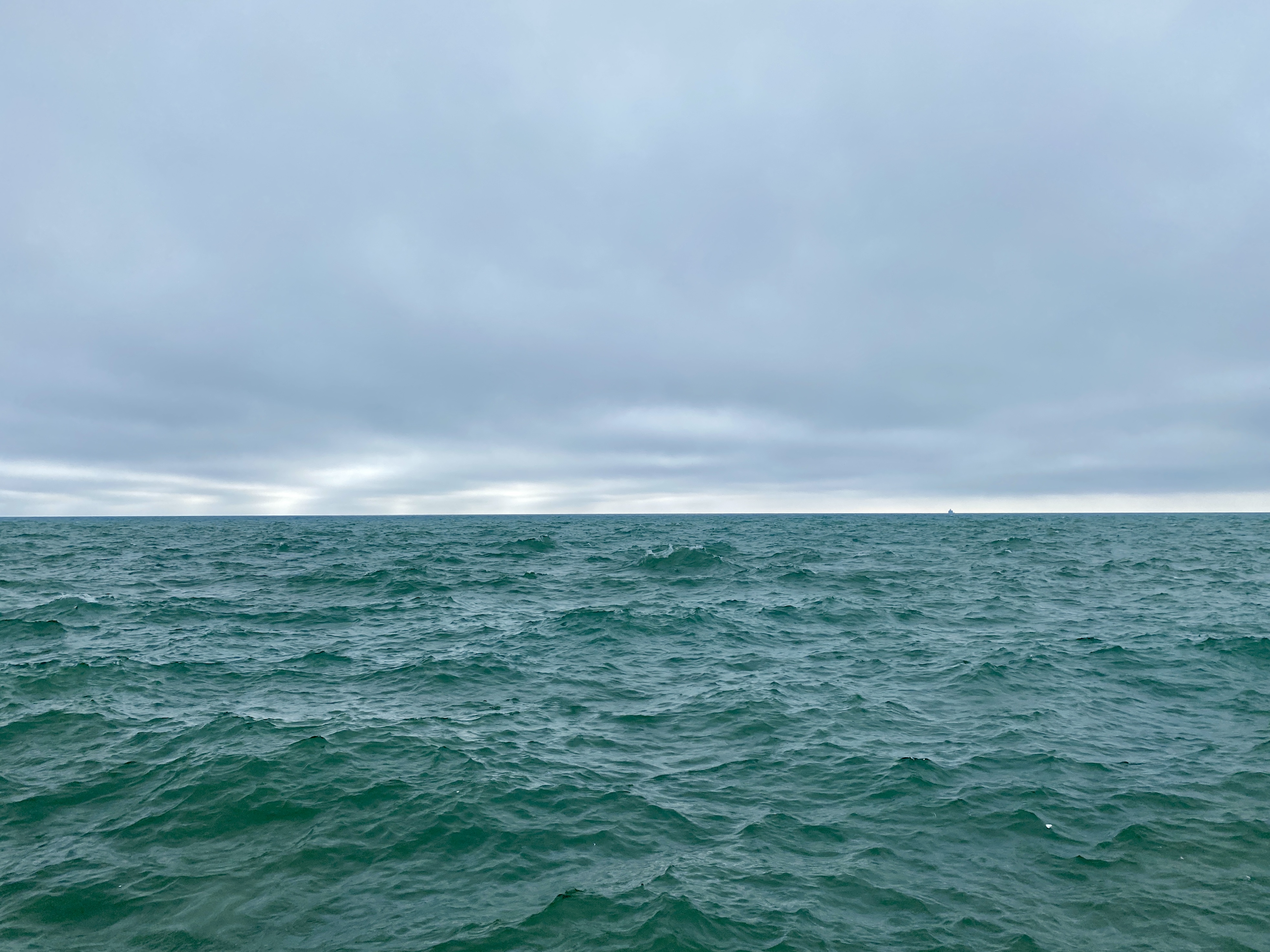A large lake under a grey clouded sky, the water surface choppy and shaded dark turquoise