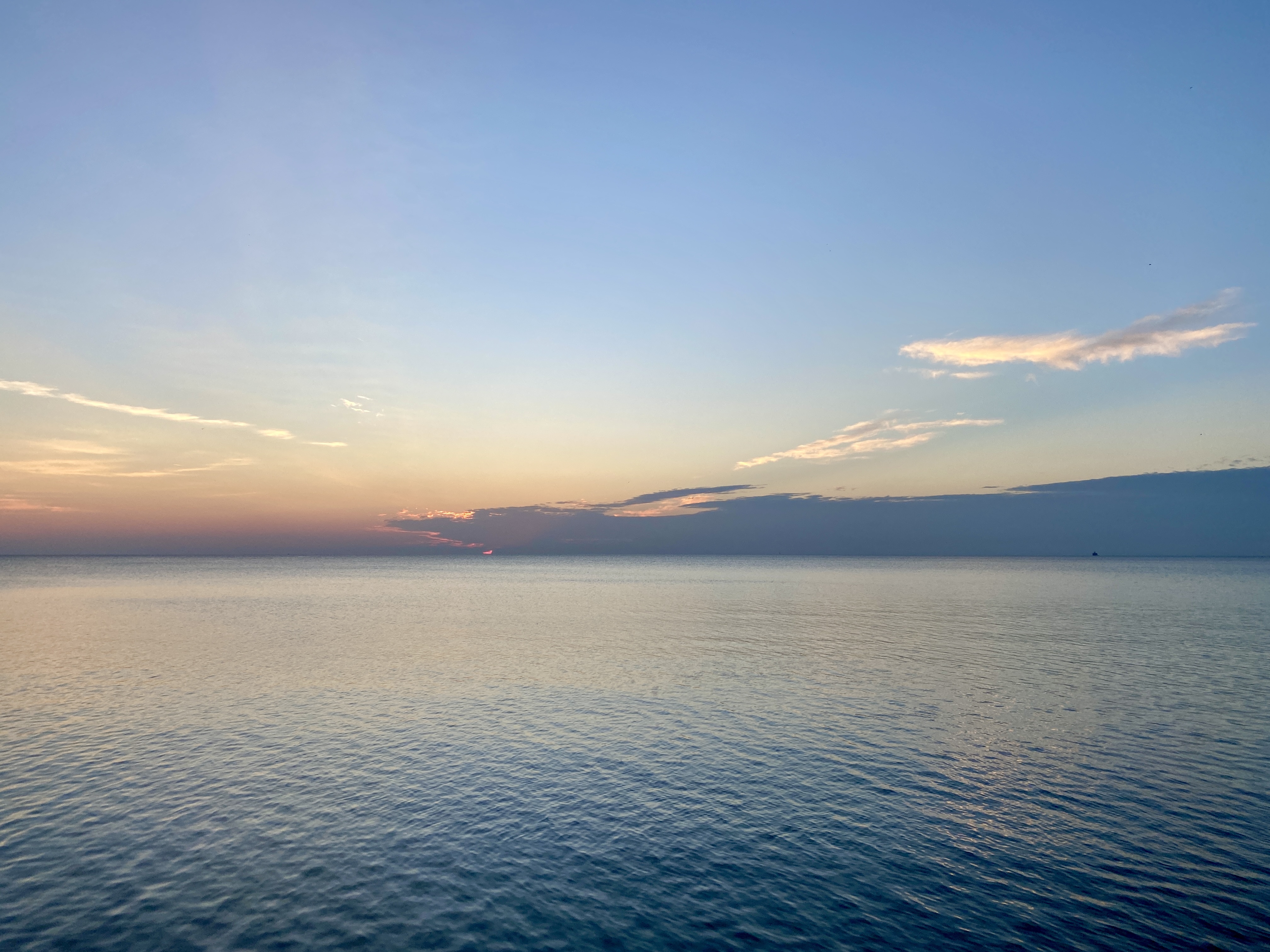 A wide lake horizon with a sweep of dark blue clouds along the water's edge, the lake surface calm and pale blue