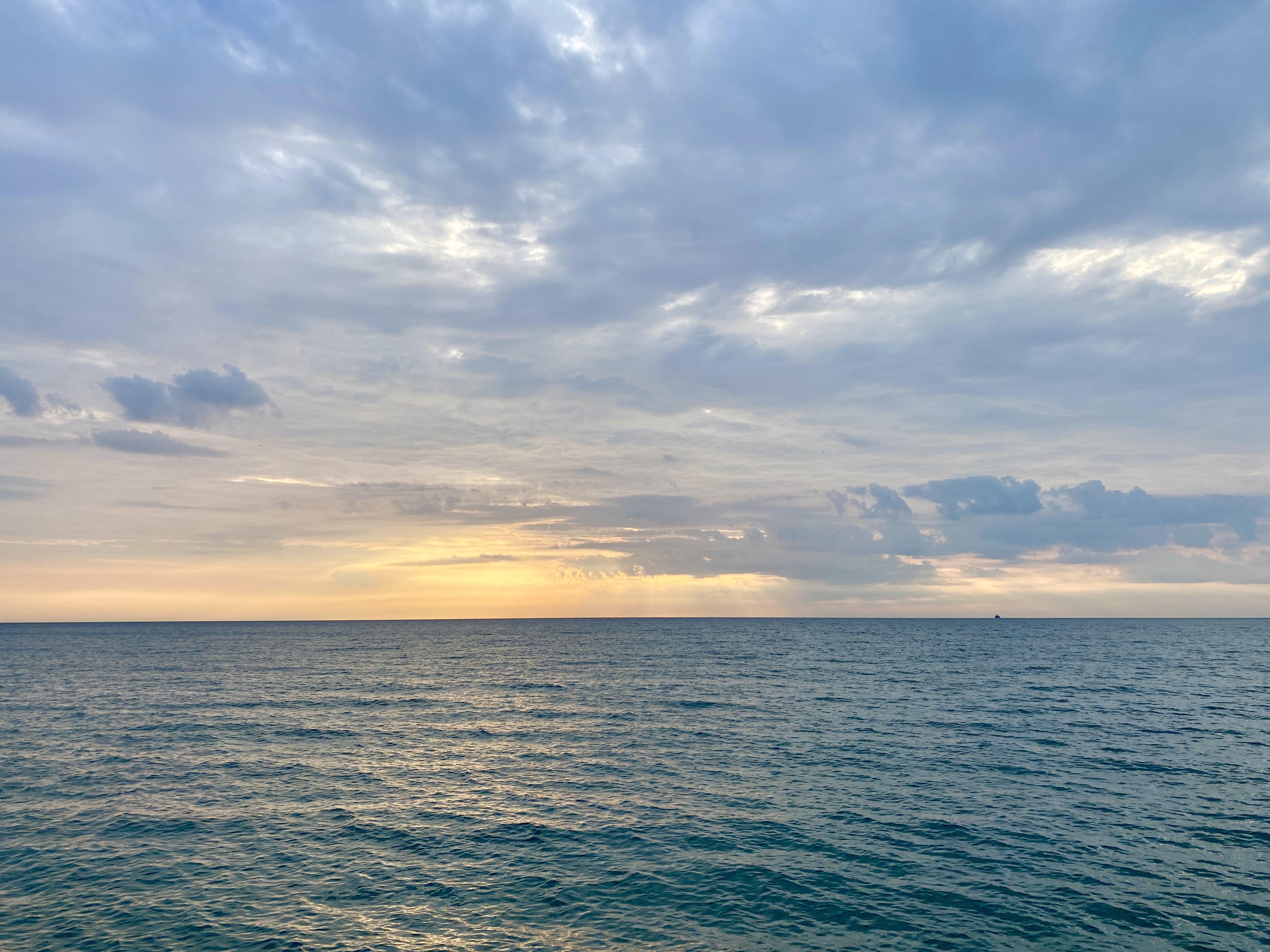 A wide lake horizon with a lightly clouded sky, orange sunrise breaking through, and a moderately calm dark blue lake surface