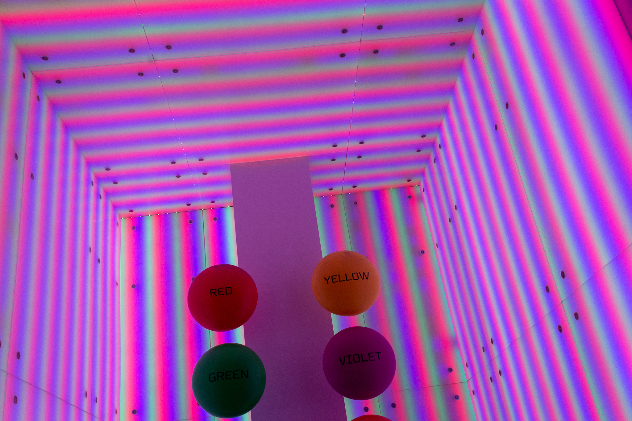 Top corners of square room lined with pink, green and yellow stripes of light with large circles labeled with different color names lined down the middle