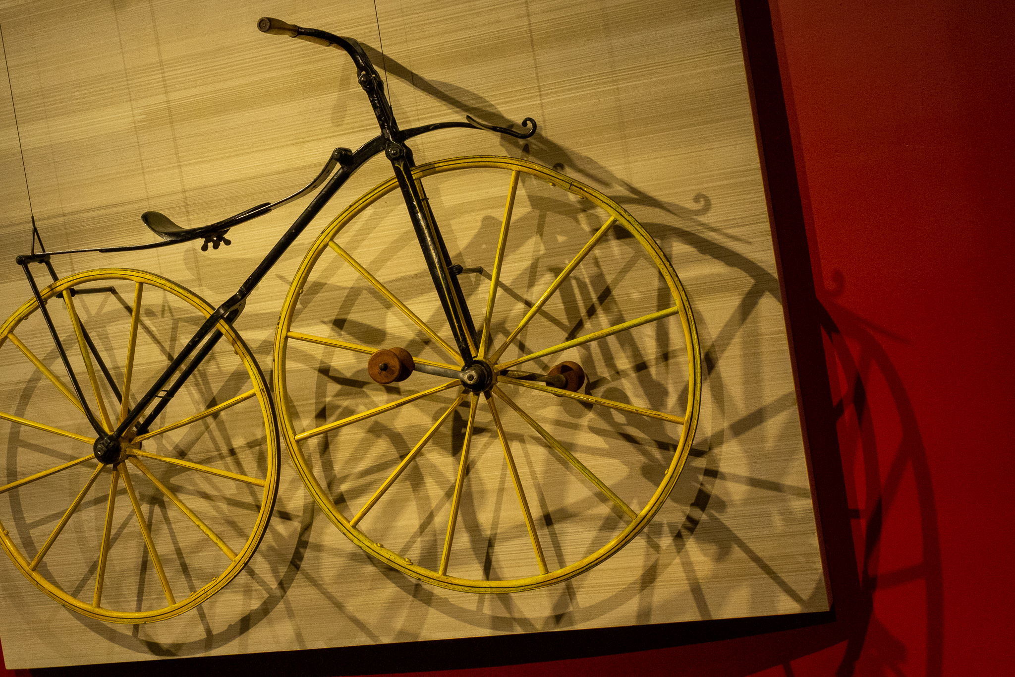 An old bicycle mounted on a museum wall with the shadows of its spokes spread on the wall behind it