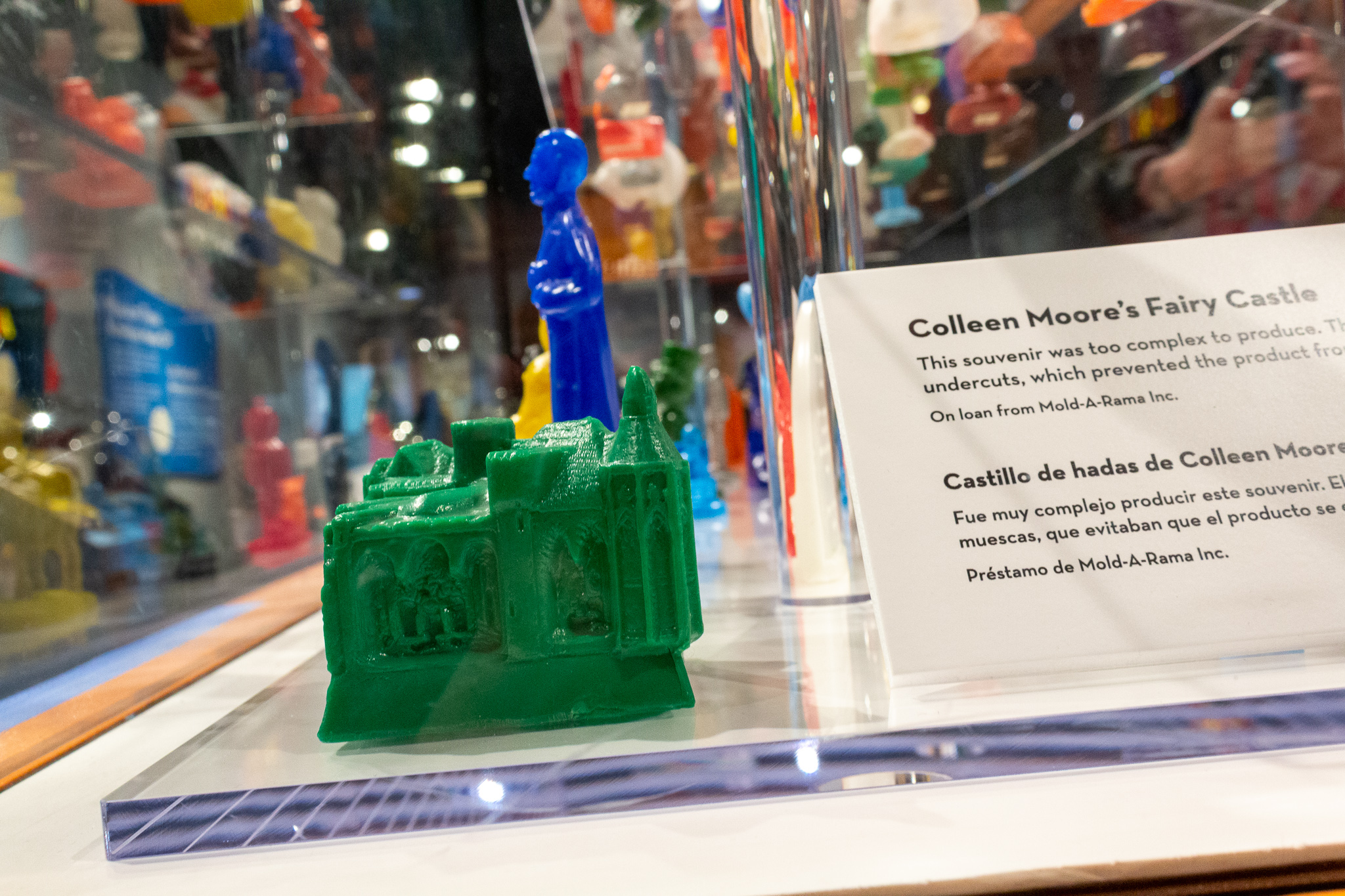 Closeup of a small green plastic figure of a dollhouse and a placard describing it as a mold of Colleen Moore's Fairy Castle