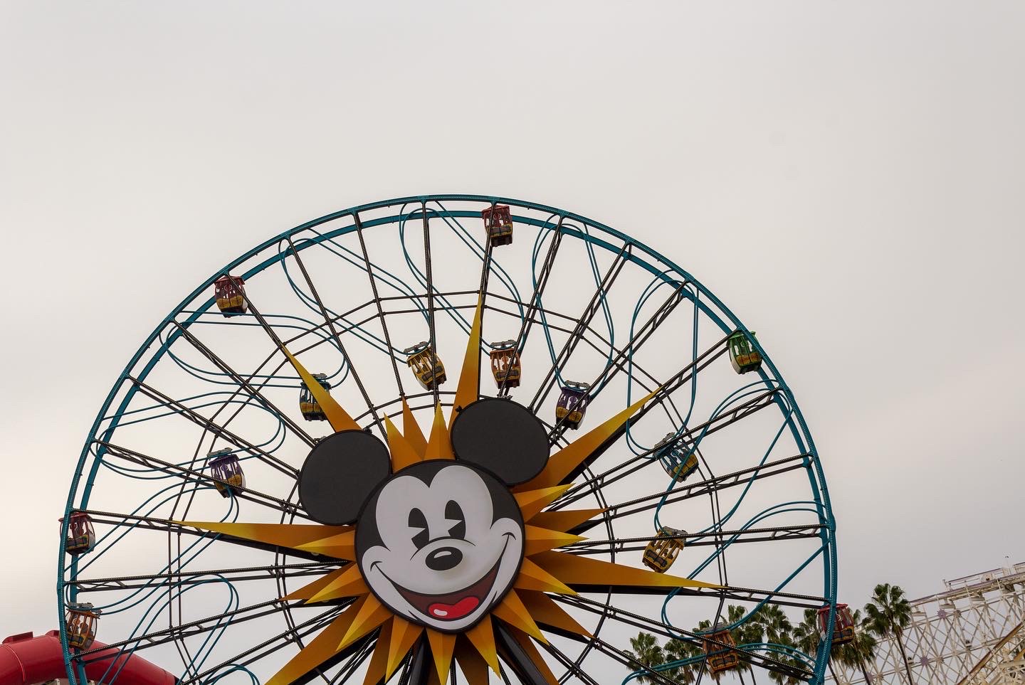 Section of large Ferris wheel with the face of Mickey Mouse at its center against a smooth grey sky