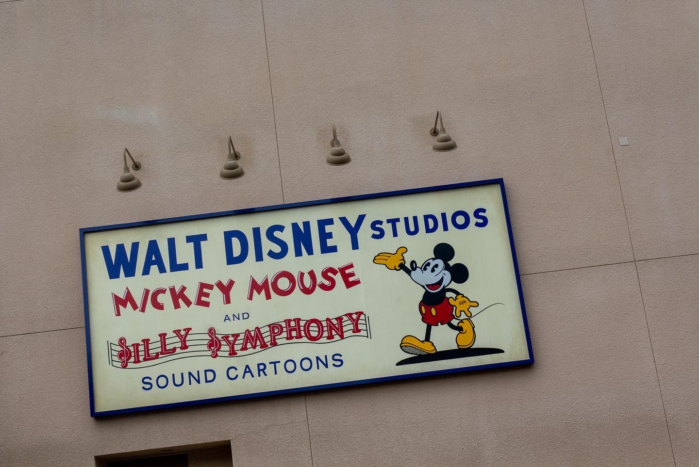 Sign on the side of a beige building that reads Walt Disney Studios Mickey Mouse and Silly Symphony Sound Cartoons with an illustration of Mickey Mouse
