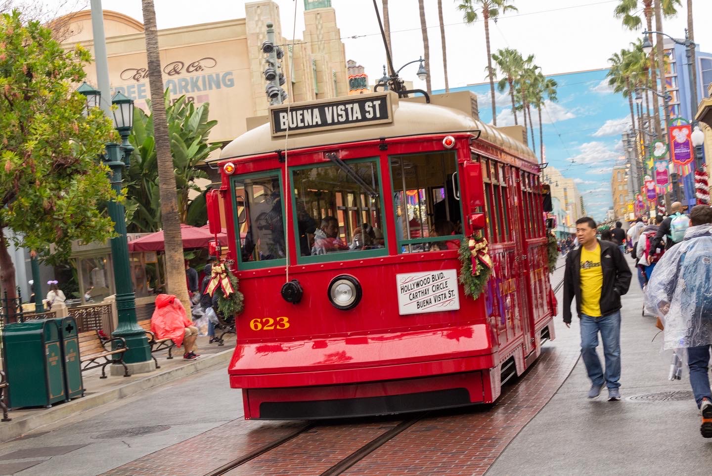 A red streetcar moves away down a theme park street, its destination sign reading Hollywood