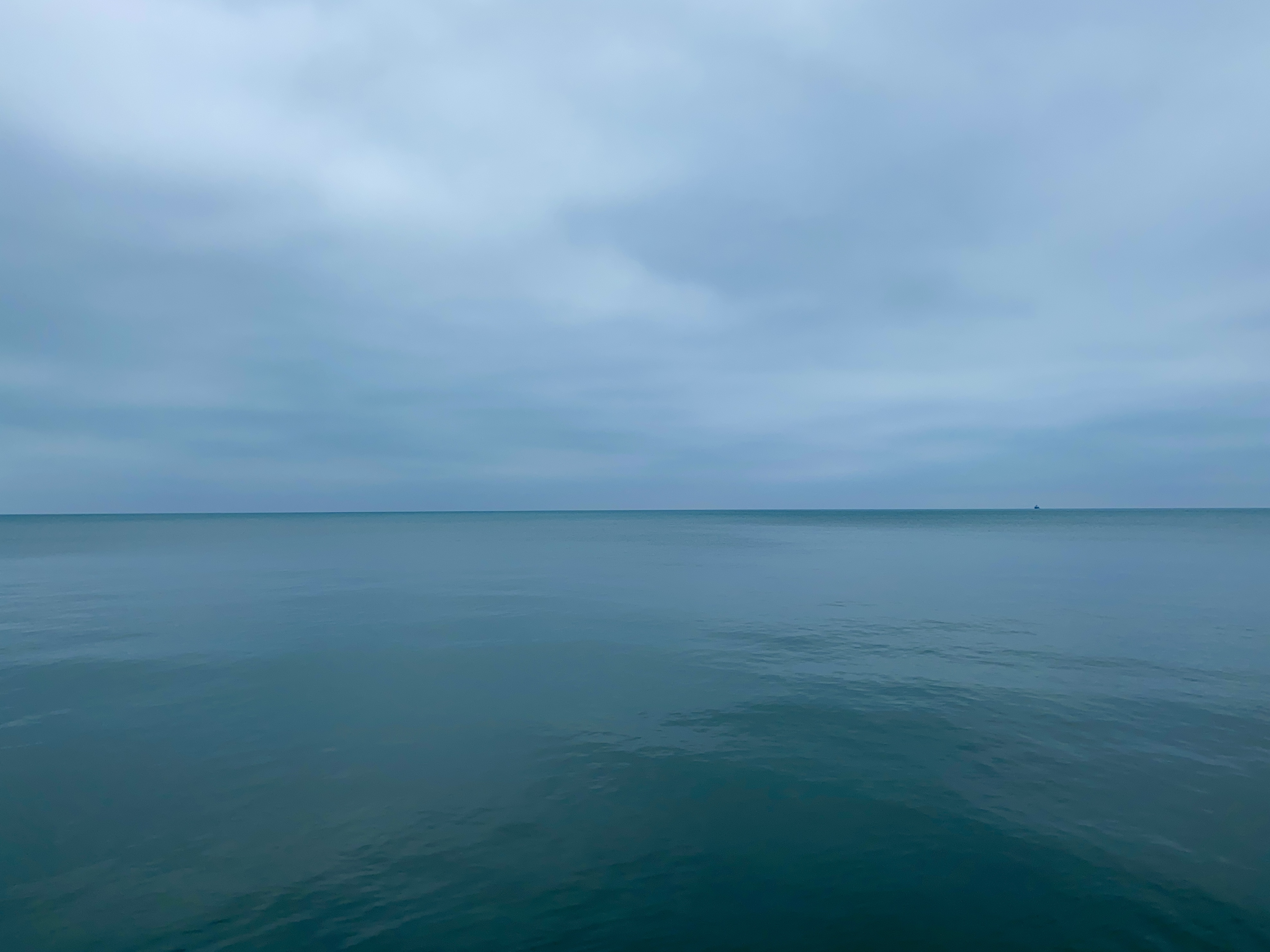 A calm lake horizon, clouded grey-blue sky above and flat dark green water below