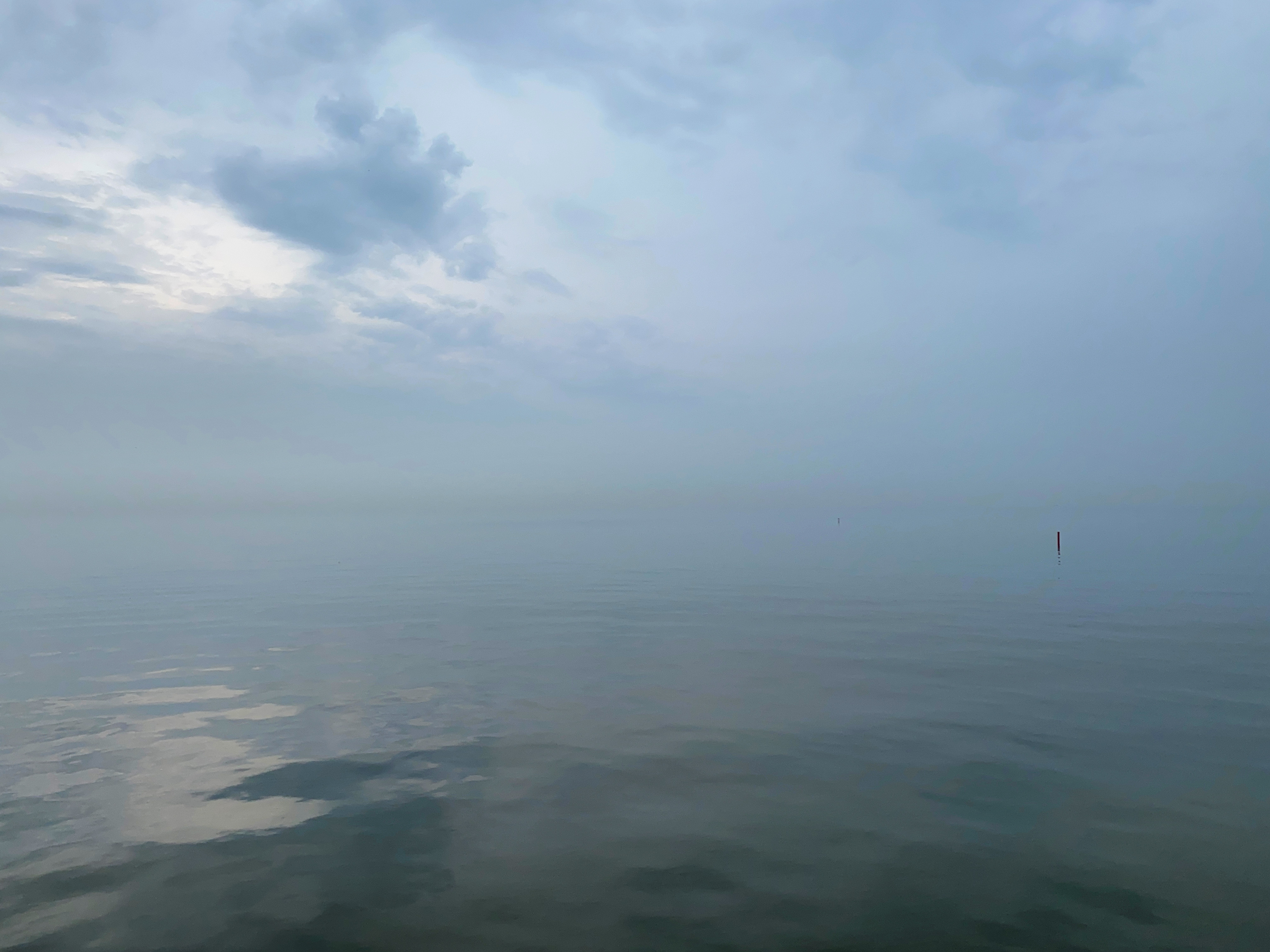 Hazy and cloudy pale blue sky above a glassy lake surface