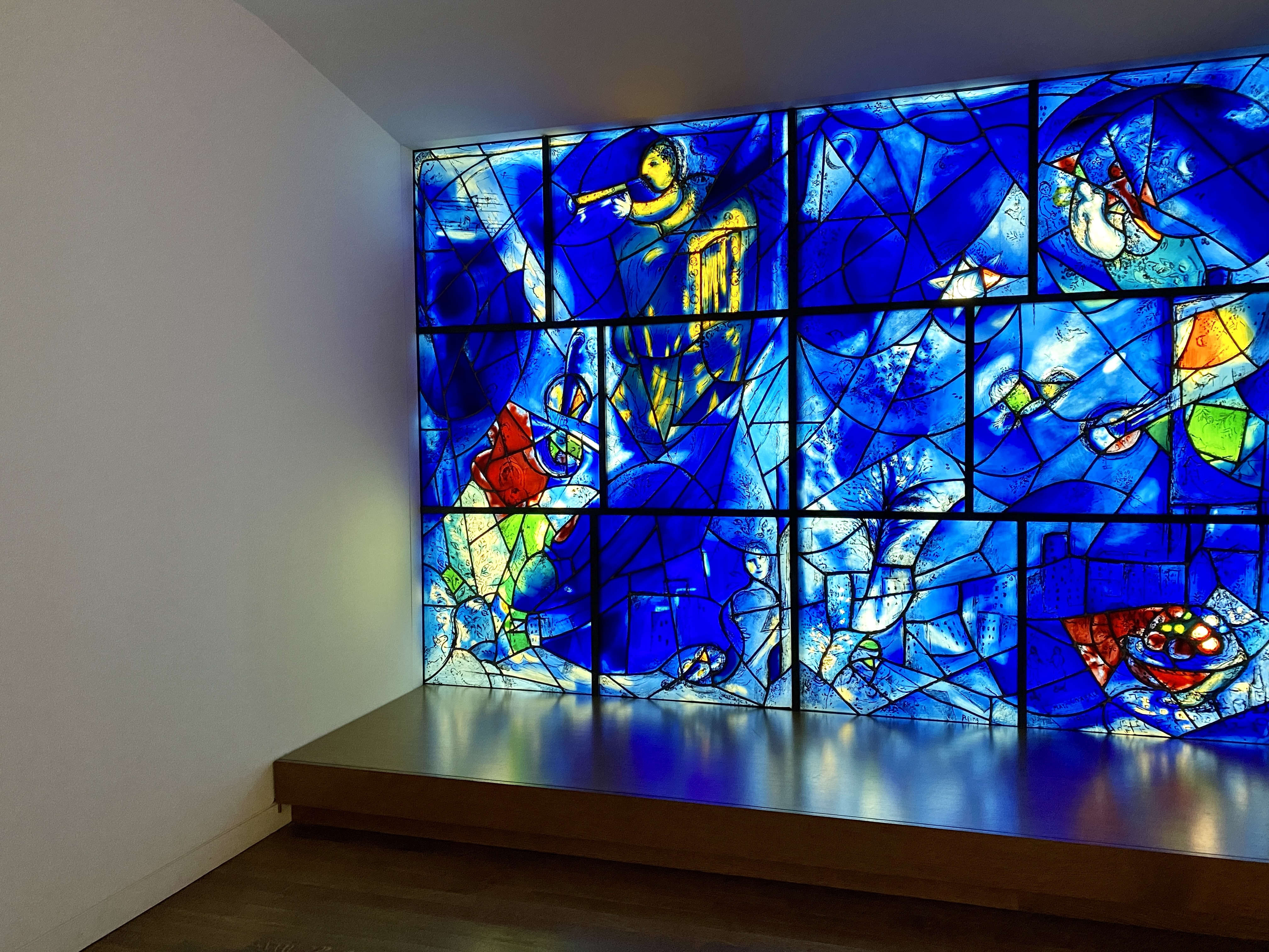 An angled view of a portion of Marc Chagall’s America Windows, stained glass panels with abstract shapes, mostly blue mixed with green and red, a yellow angel in the top corner