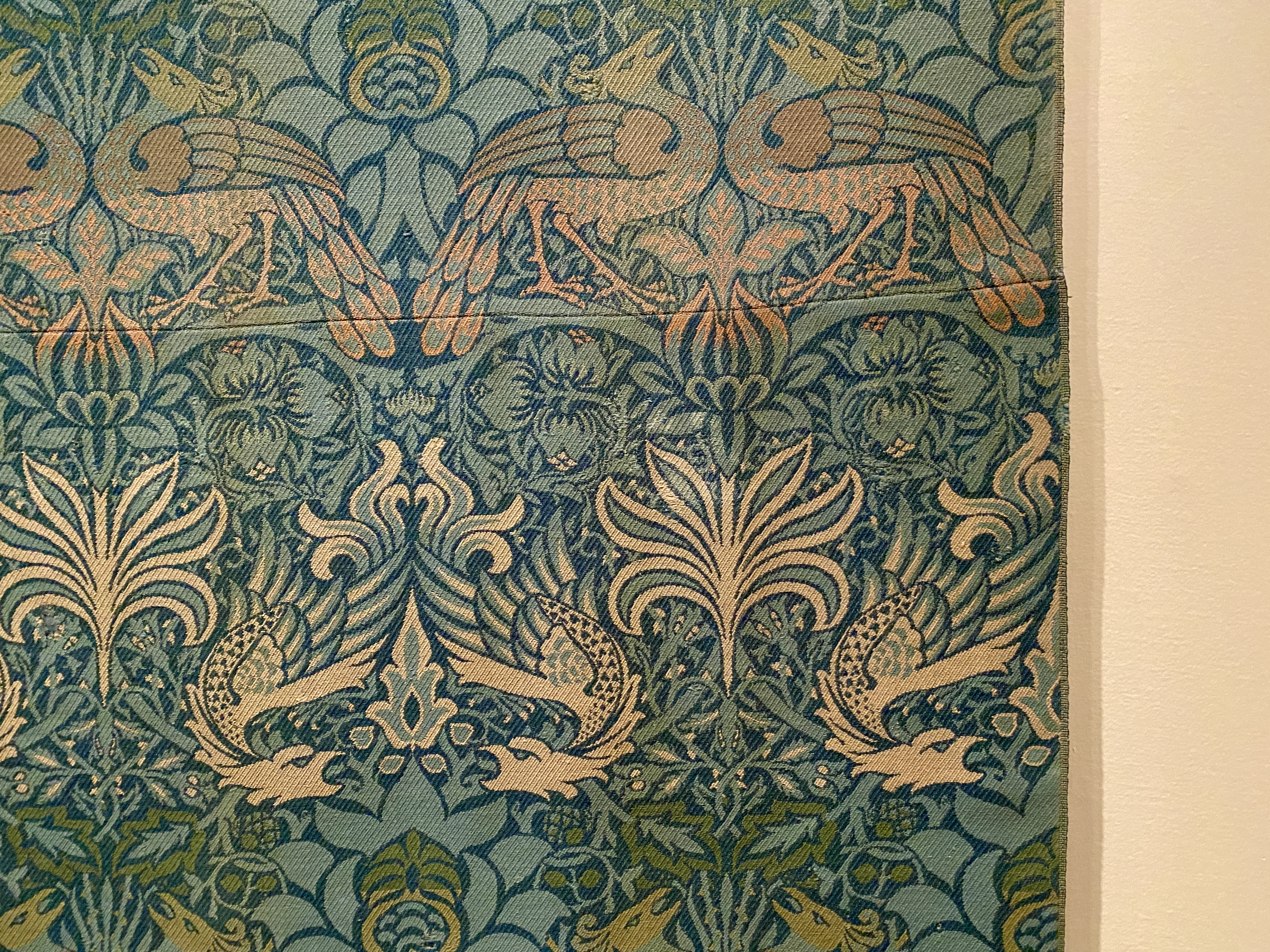Portion of antique textile with a stylized repeating design of peacocks and dragons in turquoise, green and ivory