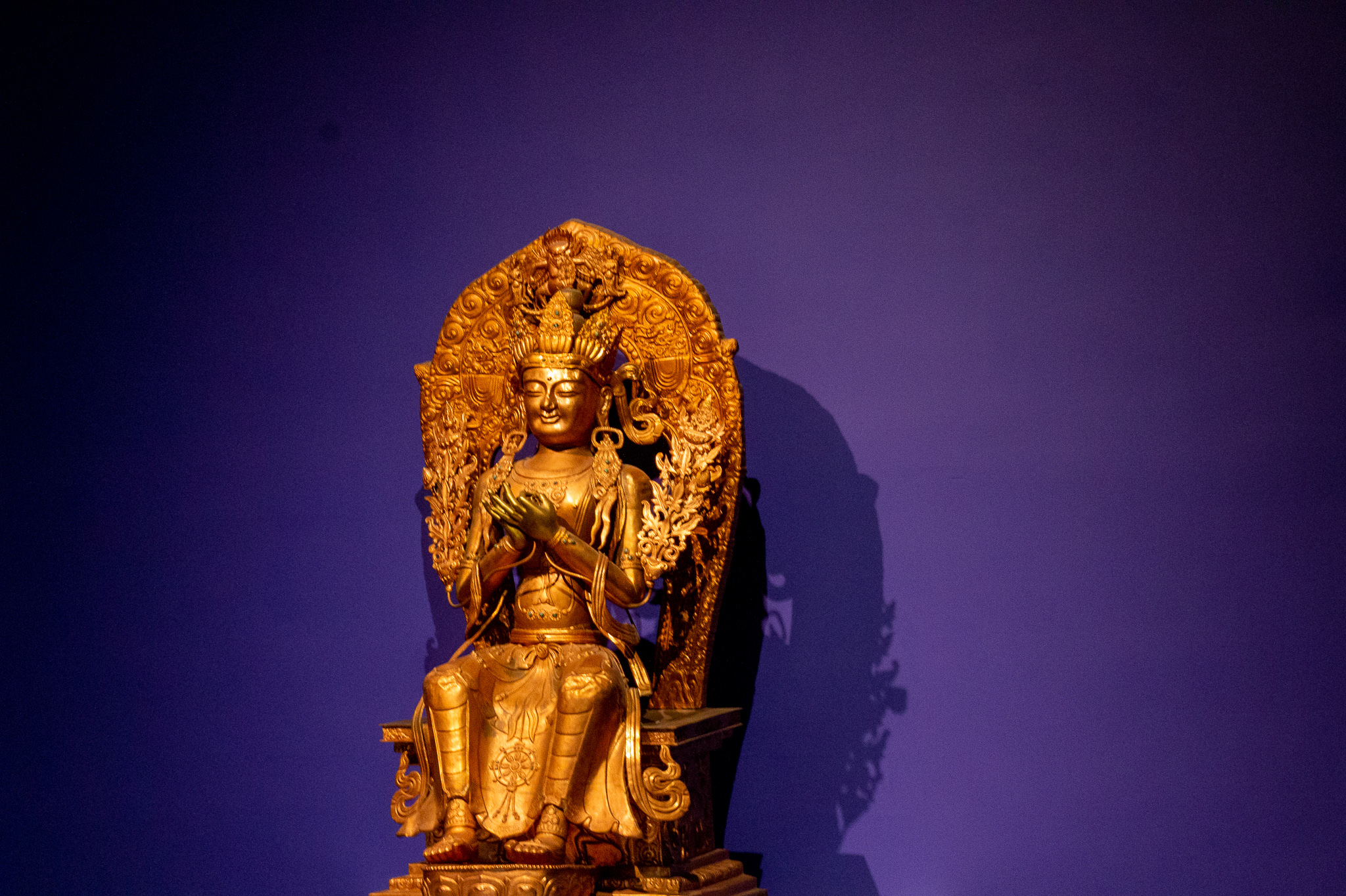 A golden figure of the Future Buddha against a deep purple wall