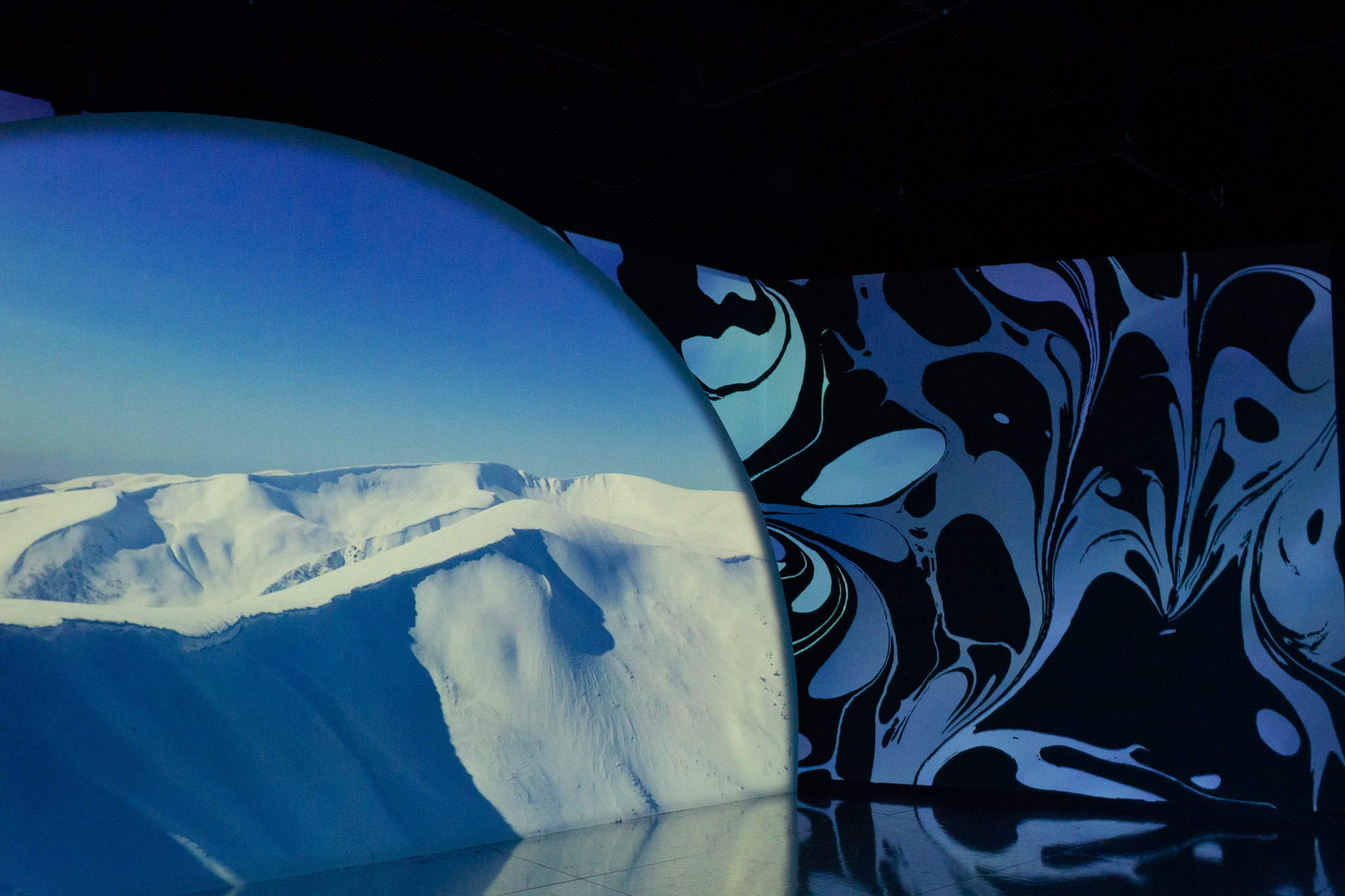 A scene of icebergs projected on a semi-circular screen next to a wall with an abstract blue wave design