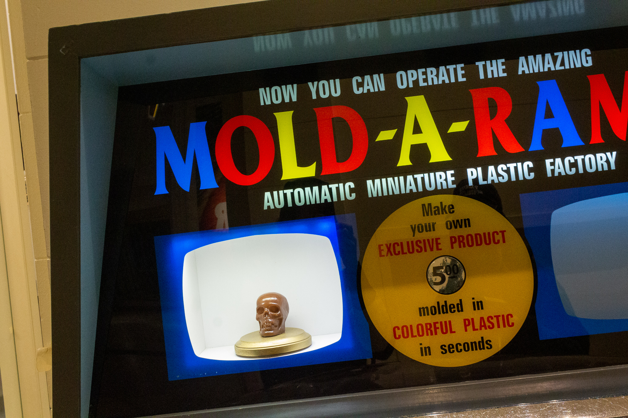 The top portion of a Mold-A-Rama plastic injection machine displaying a small brown skull as example plastic figure