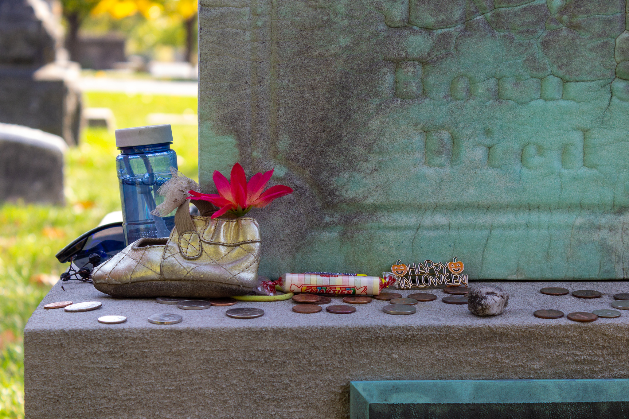 The edge of a young girl's gravestone dotted with candy, toys and a Happy Halloween pin left for her