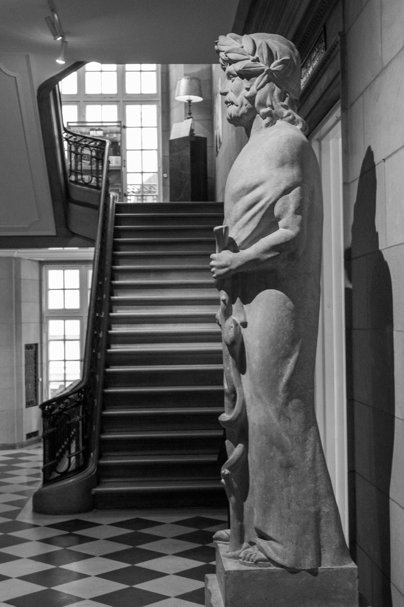 A large stone statue in profile in front of a marble stairway leading to the second story of the mansion