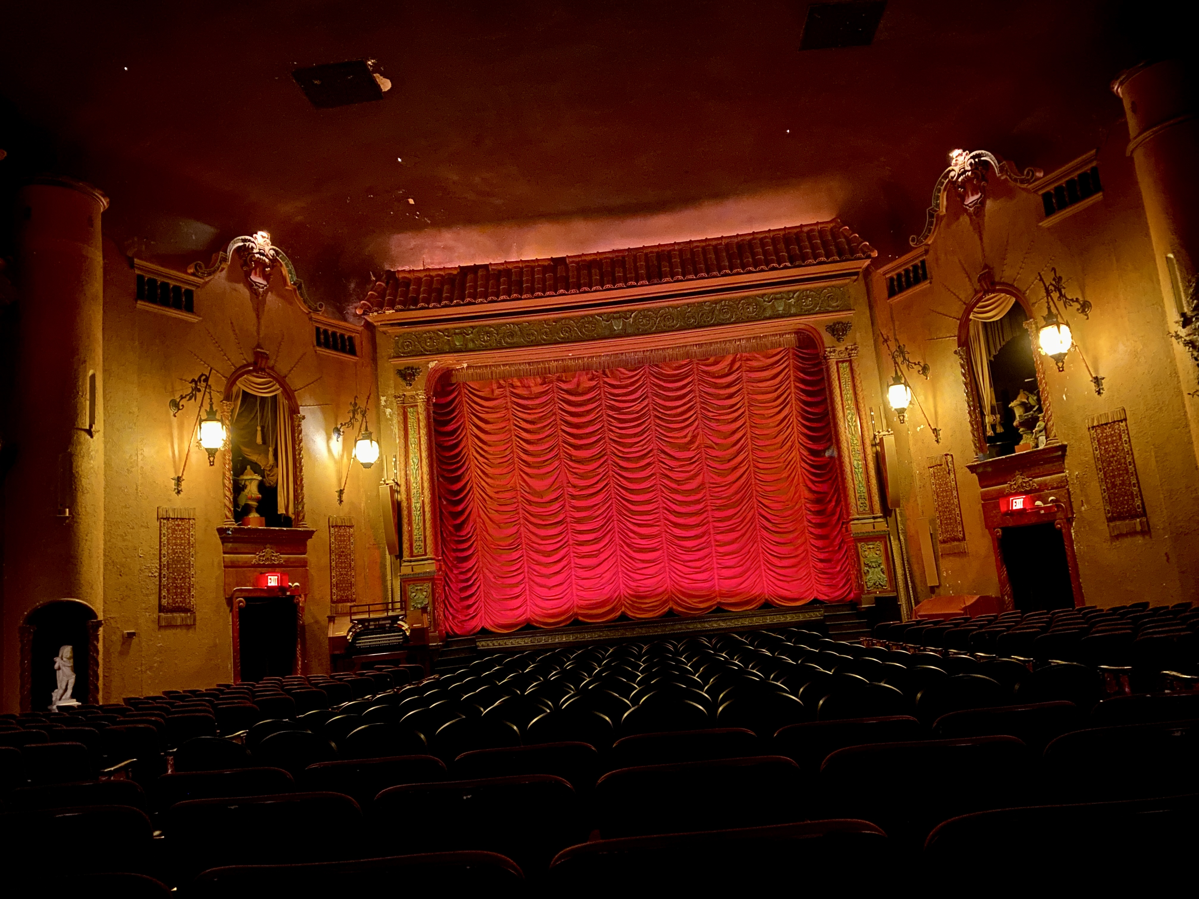 A canted view of an empty vintage movie theater styled like a Italian piazza with a red curtain hanging in front of the screen
