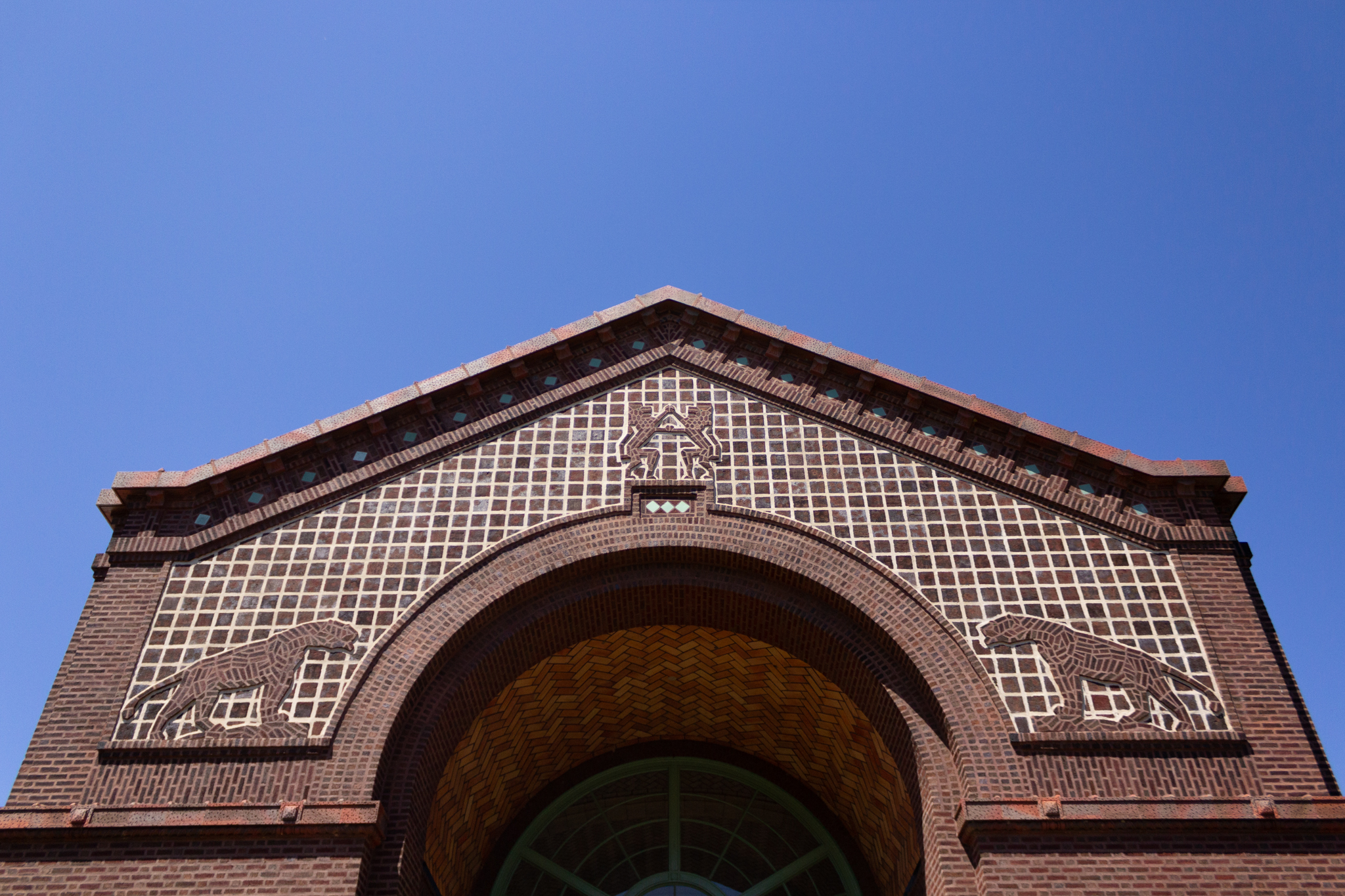 The roof of a building decorated with tiles and lion reliefs against a bright blue sky